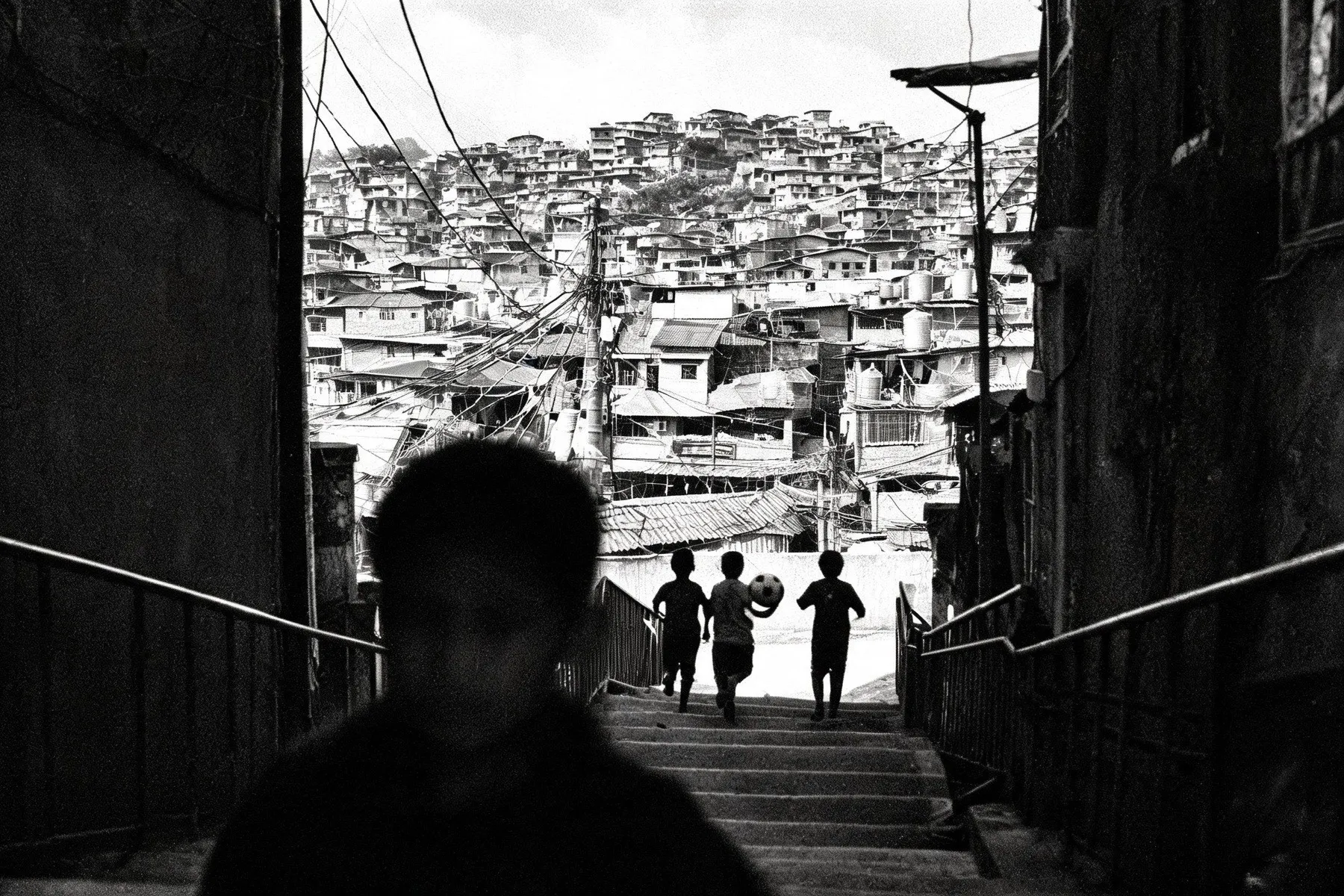 Drie kinderen lopen met een bal een trap af, met een favela tegen de heuvel op de achtergrond
