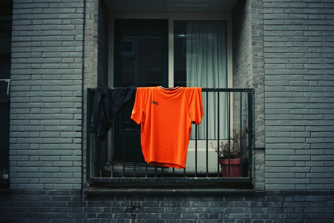 Een fel oranje voetbalshirt hangt over de reling van een balkon van een Nederlandse flat
